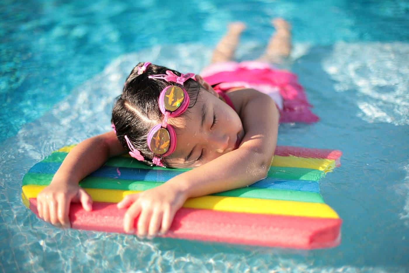 A young girl holding a swimming kickboard at the edge of a pool